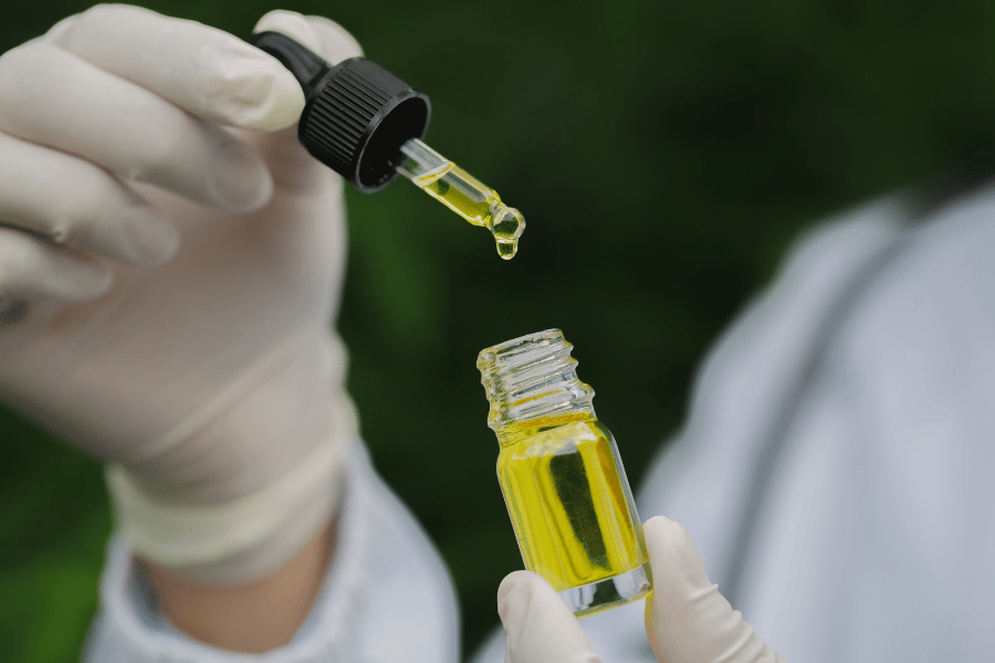 Golden cannabis-infused oil being dispensed with dropper into glass bottle, illustrating infused oil color and clarity differences