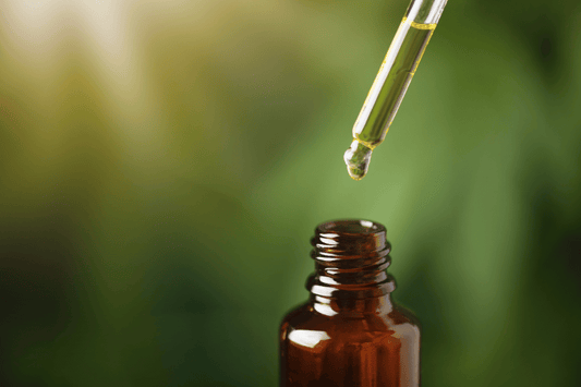 Dropper dispensing golden CBD oil into a small amber glass bottle, with a green blurred background.