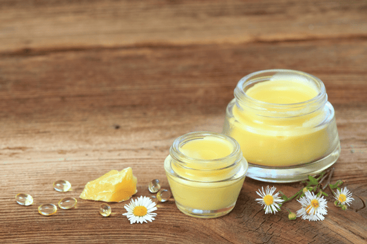 Two glass jars of yellow cannabis-infused body balm with chamomile flowers and shea butter on a wooden surface.