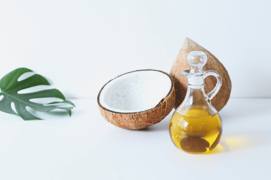 Glass jar of coconut oil beside a halved coconut on a white surface, styled for cannabis infusion blog.