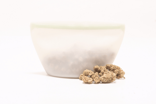 White ceramic bowl next to trimmed cannabis flower, placed on a white background for infusion preparation.