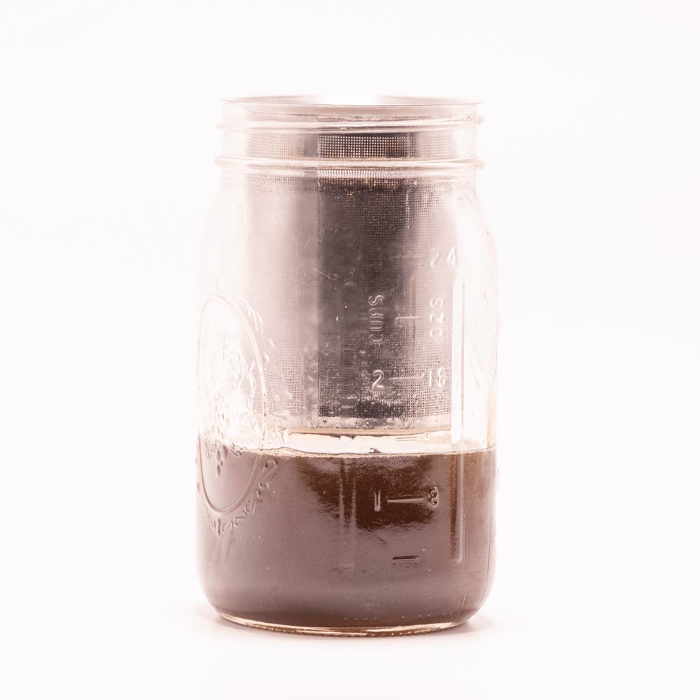 Golden infusion being strained into a glass jar